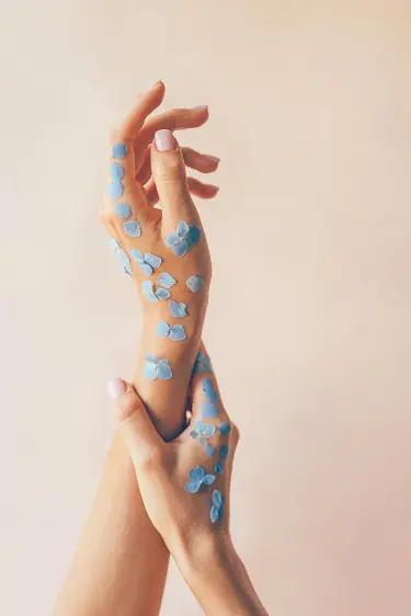 Жіночі руки з пелюстками блакитних квітів та з пастельним манікюром