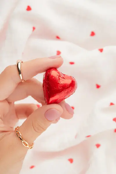 Жіноча рука з нюдовим манікюром тримає цукерку у формі серця